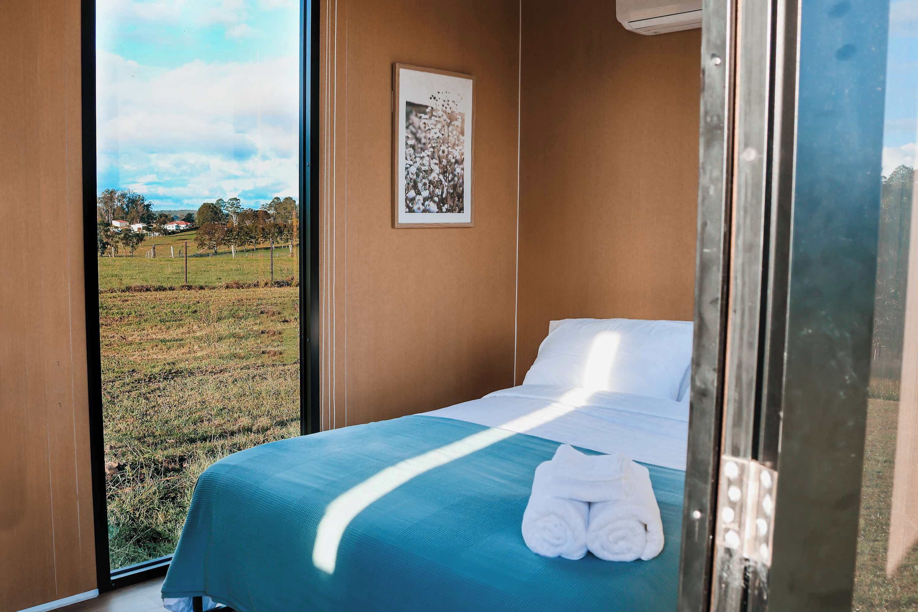 A room with a bed, a framed picture on the wall, and a view of a grassy field.