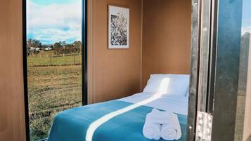 A room with a bed, a framed picture on the wall, and a view of a grassy field.