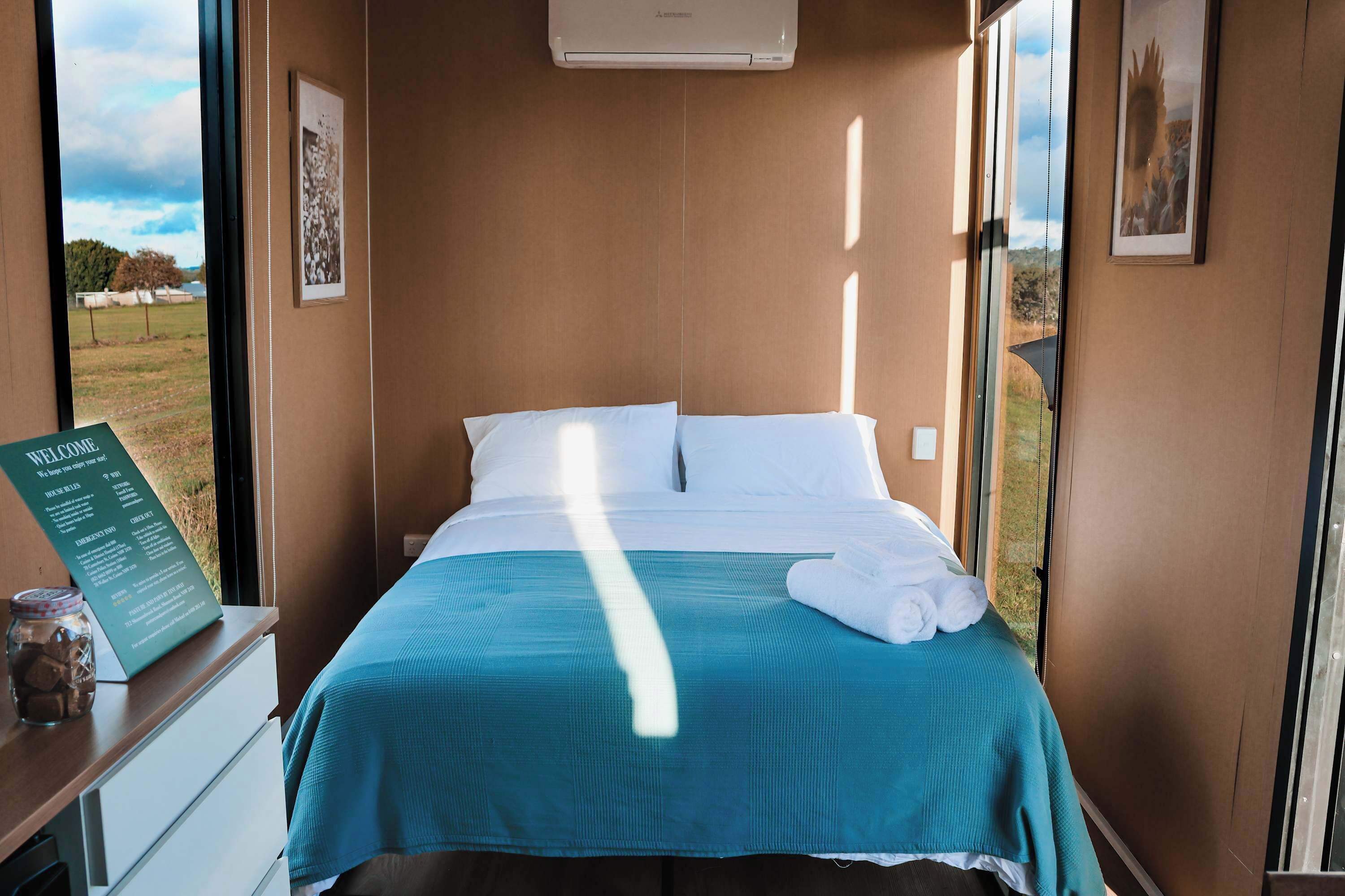 A hotel room with a bed, a window, a wall-mounted air conditioner, and a welcome sign.