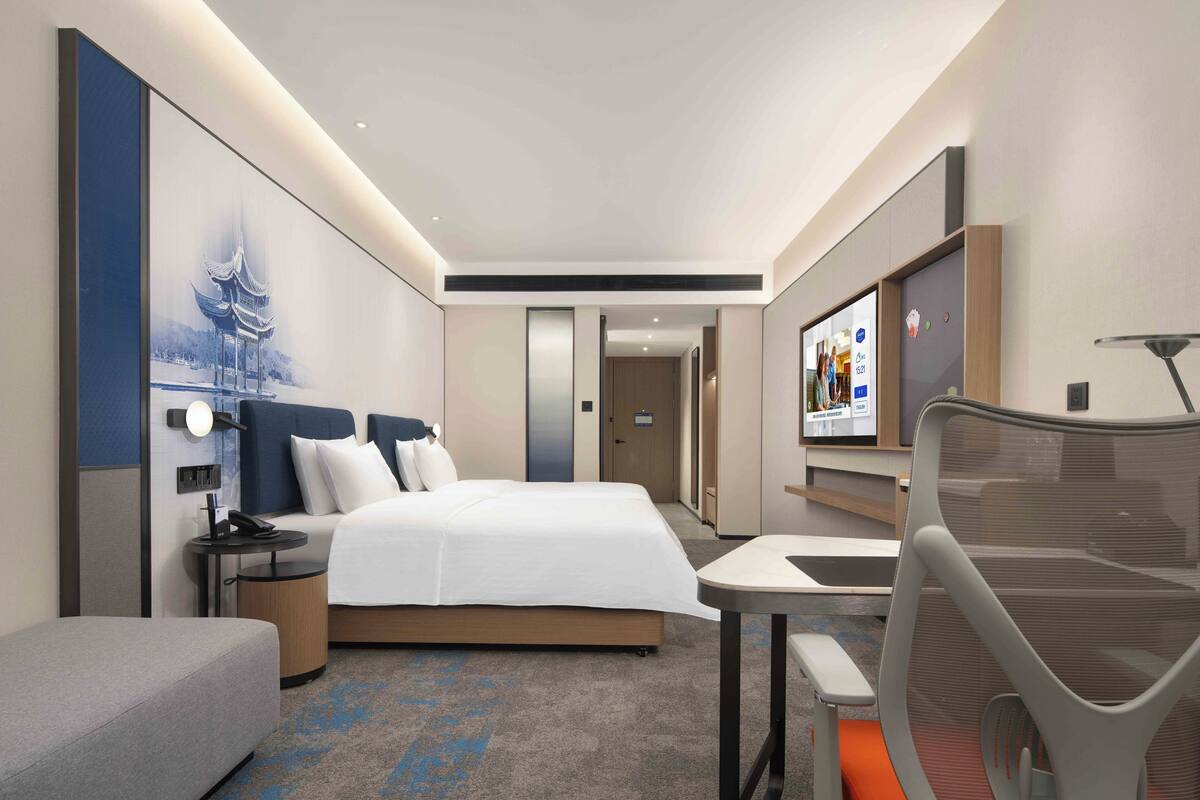 A modern hotel room with a bed, bedside table, lamp, and a TV on the wall.