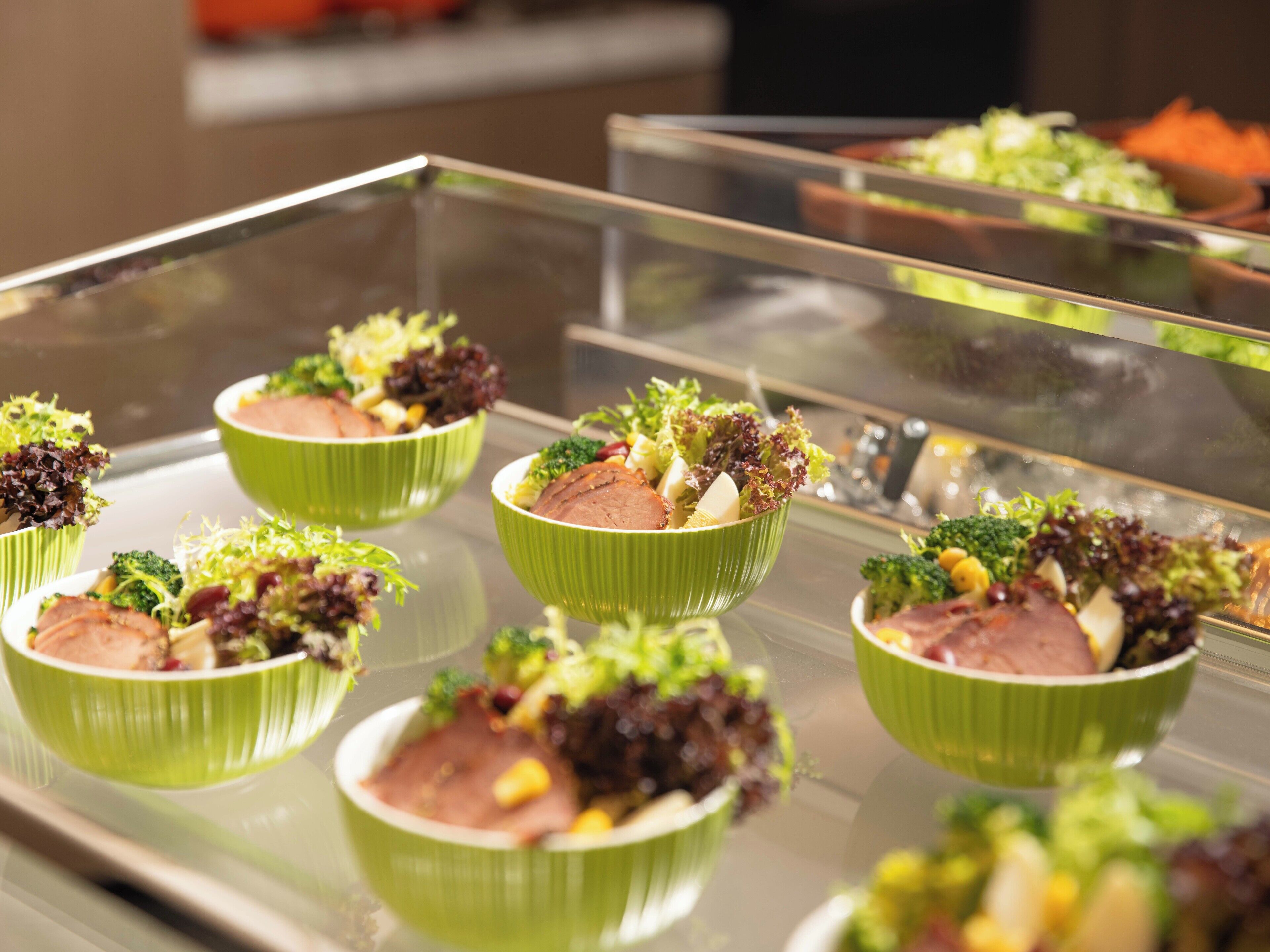 Un buffet proposant divers plats, notamment des salades et des viandes, servis dans des plats verts.
