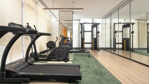 Une salle de sport équipée de matériel d’exercice, notamment des tapis de course et une machine de musculation, ainsi qu’un miroir qui reflète l’espace.