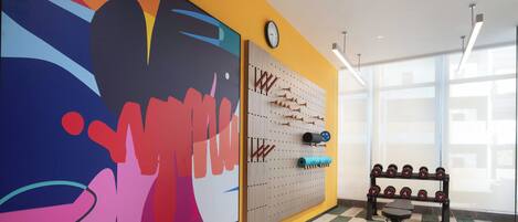 A gym with a colorful wall mural, a wall-mounted dumbbell rack, and a scale on the floor.