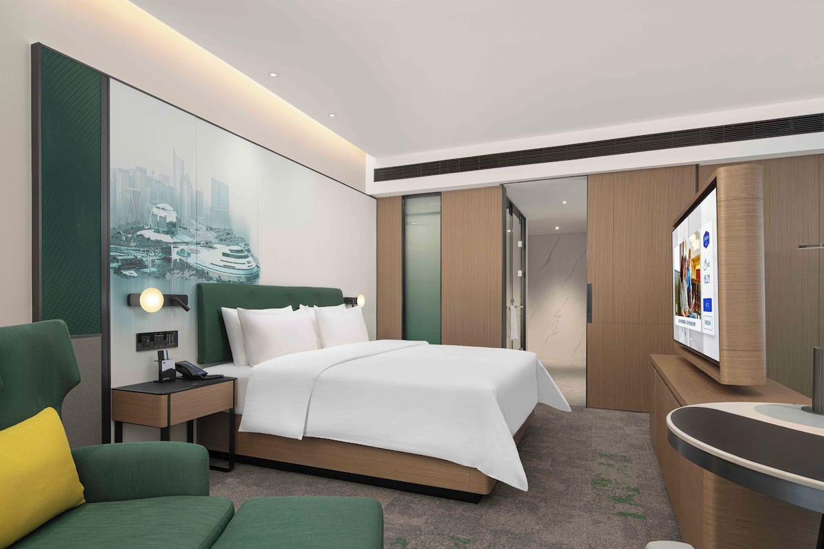 A modern hotel room with a bed, a desk, a chair, a TV, and a bathroom area.