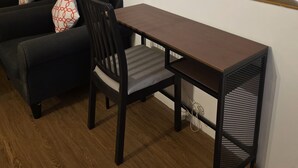 Un espace de vie compact doté d’un plancher en bois foncé, d’un canapé noir agrémenté de coussins à motifs, d’une petite table en bois et d’une chaise.