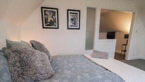A bedroom with a large bed, two framed pictures on the wall, and a view into the adjacent kitchen area. - The Loft - 96B (Coleraine)