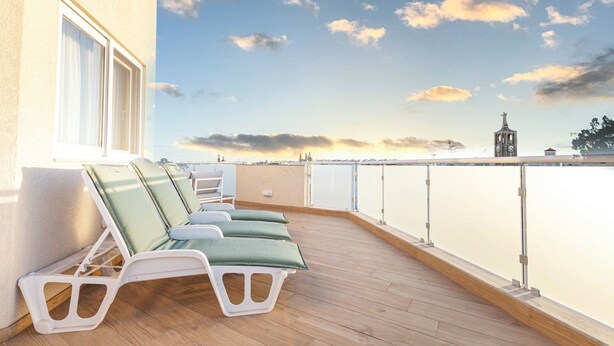 Een terras met lounge fauteuils en uitzicht op een stadshemel bij zonsondergang.