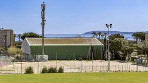 Un edificio con tejado verde, rodeado por una zona vallada con vistas despejadas al mar y montañas al fondo.