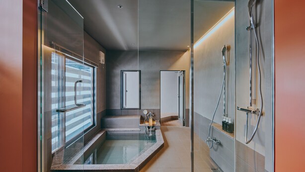 Een moderne badkamer met een glazen hottub, een douchegedeelte en een zichtbare deur naar een andere kamer.