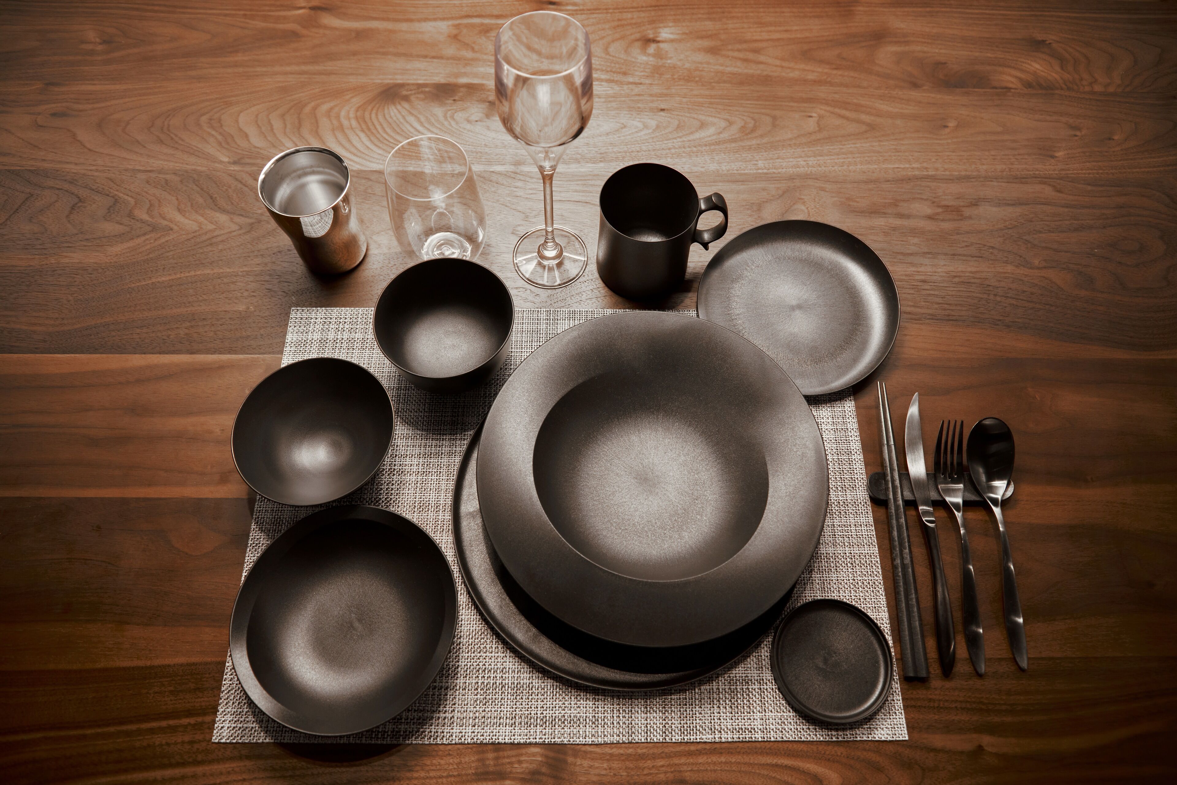 A wooden table with various dinnerware items including plates, bowls, a wine glass, and cutlery.