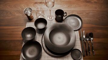 A wooden table with various dinnerware items including plates, bowls, a wine glass, and cutlery.