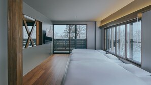 Een moderne slaapkamer met een groot bed, houten vloer en grote ramen met uitzicht op een besneeerd landschap.