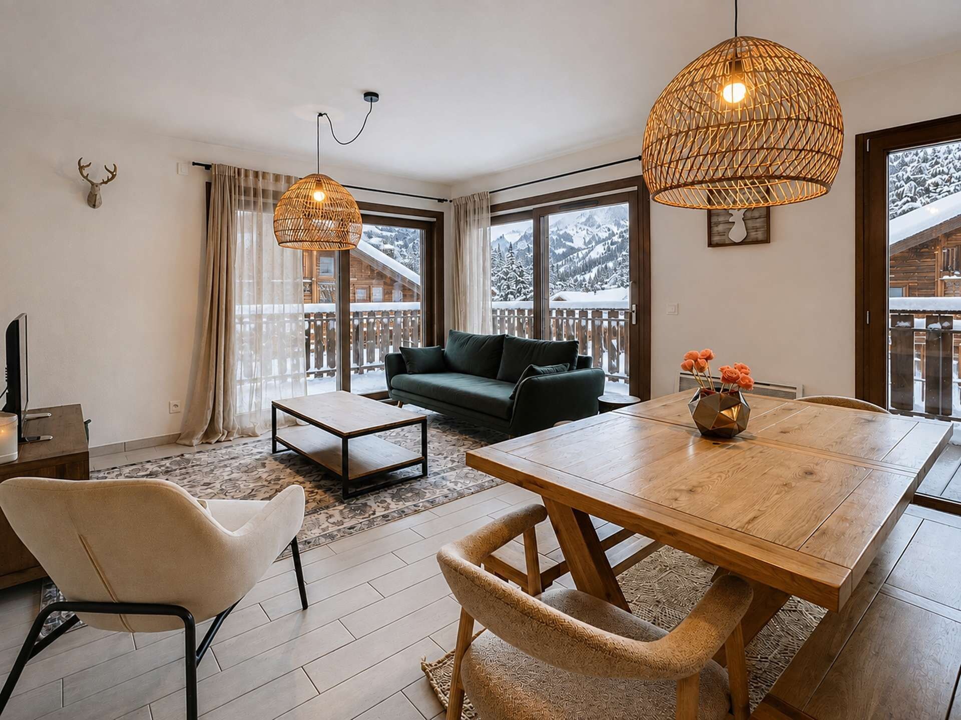 Un salon moderne avec un canapé, une table à manger et une table basse. On y trouve deux lampes suspendues et une fenêtre donnant sur un paysage enneigé.