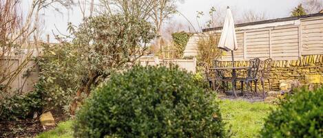 A garden with a stone wall, a wooden fence, and a metal table with chairs.