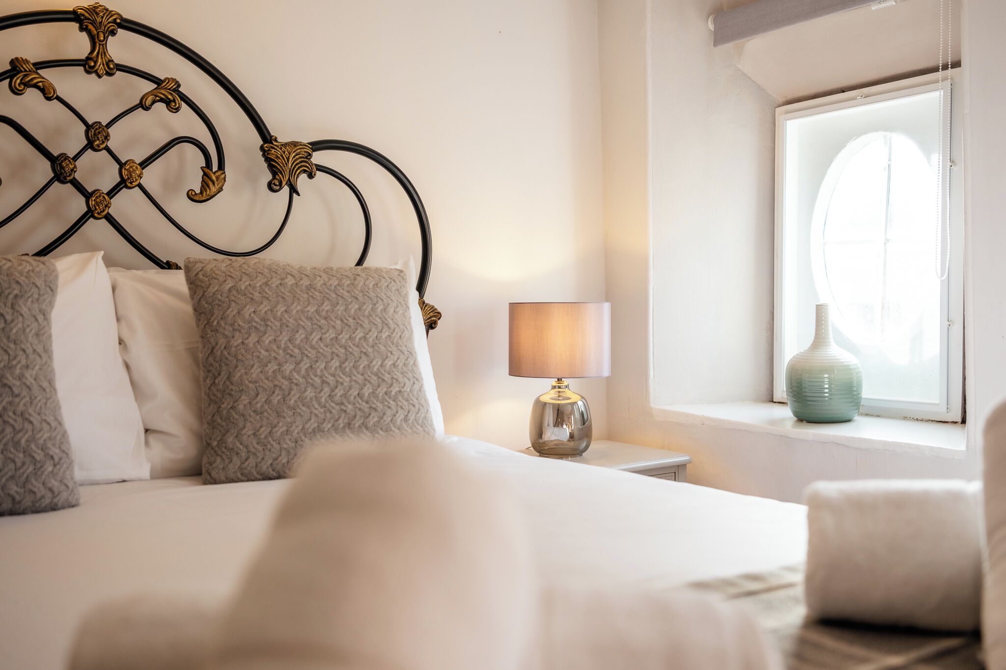 A neatly made bed with a decorative headboard, a bedside lamp, and a vase on the windowsill.