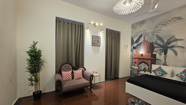 Una sala de estar con un sofá, una silla, una mesita con bebidas, una planta en maceta y un mural en la pared.