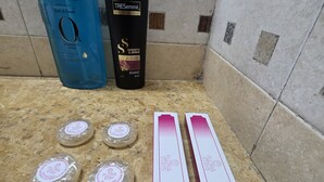 Una encimera de baño con artículos de aseo, incluyendo crema corporal Pears, champú TRESemmé, jabón Flora Stay y kits dentales.