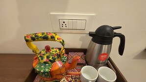 Una bandeja con un colorido hervidor, dos tazas blancas y un termo de acero inoxidable.