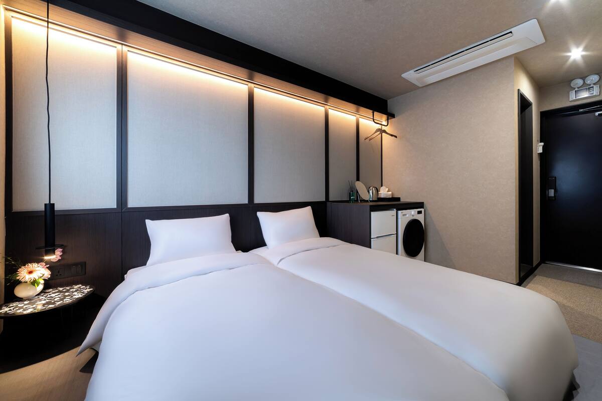 Ein modernes Hotelzimmer mit einem großen Bett, einem Nachttisch mit Lampe, einem Spiegel und einer integrierten Waschmaschine.