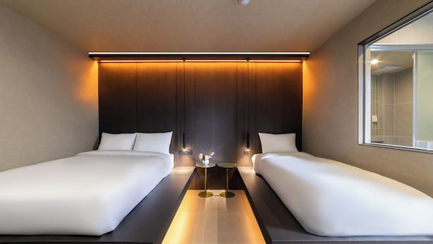 Ein modernes Hotelzimmer mit zwei Einzelbetten, einem kleinen Tisch mit einer Vase und einem großen Fenster.