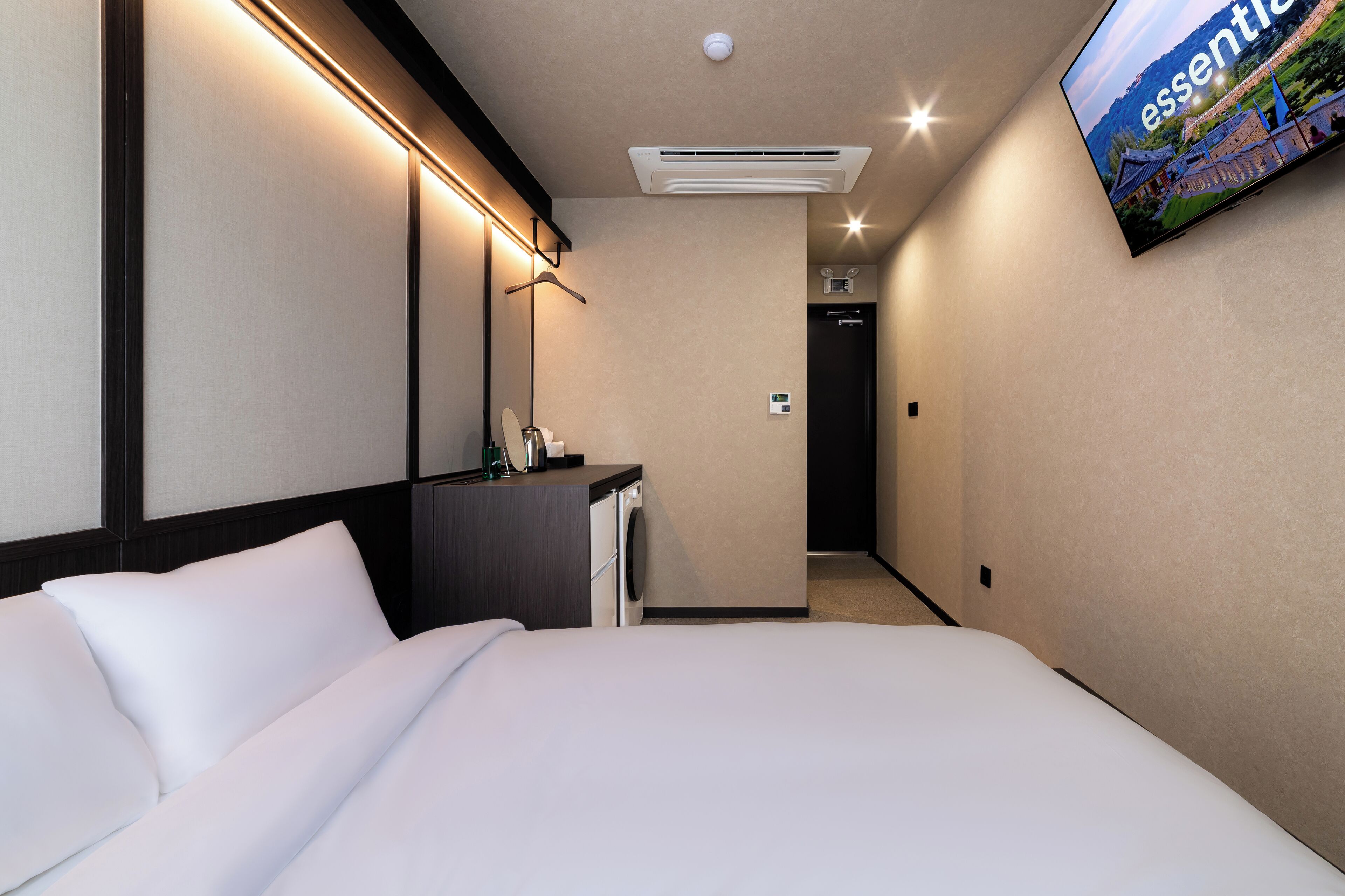 Ein Hotelzimmer mit Bett, Schreibtisch, Spiegel und Fernseher an der Wand.
