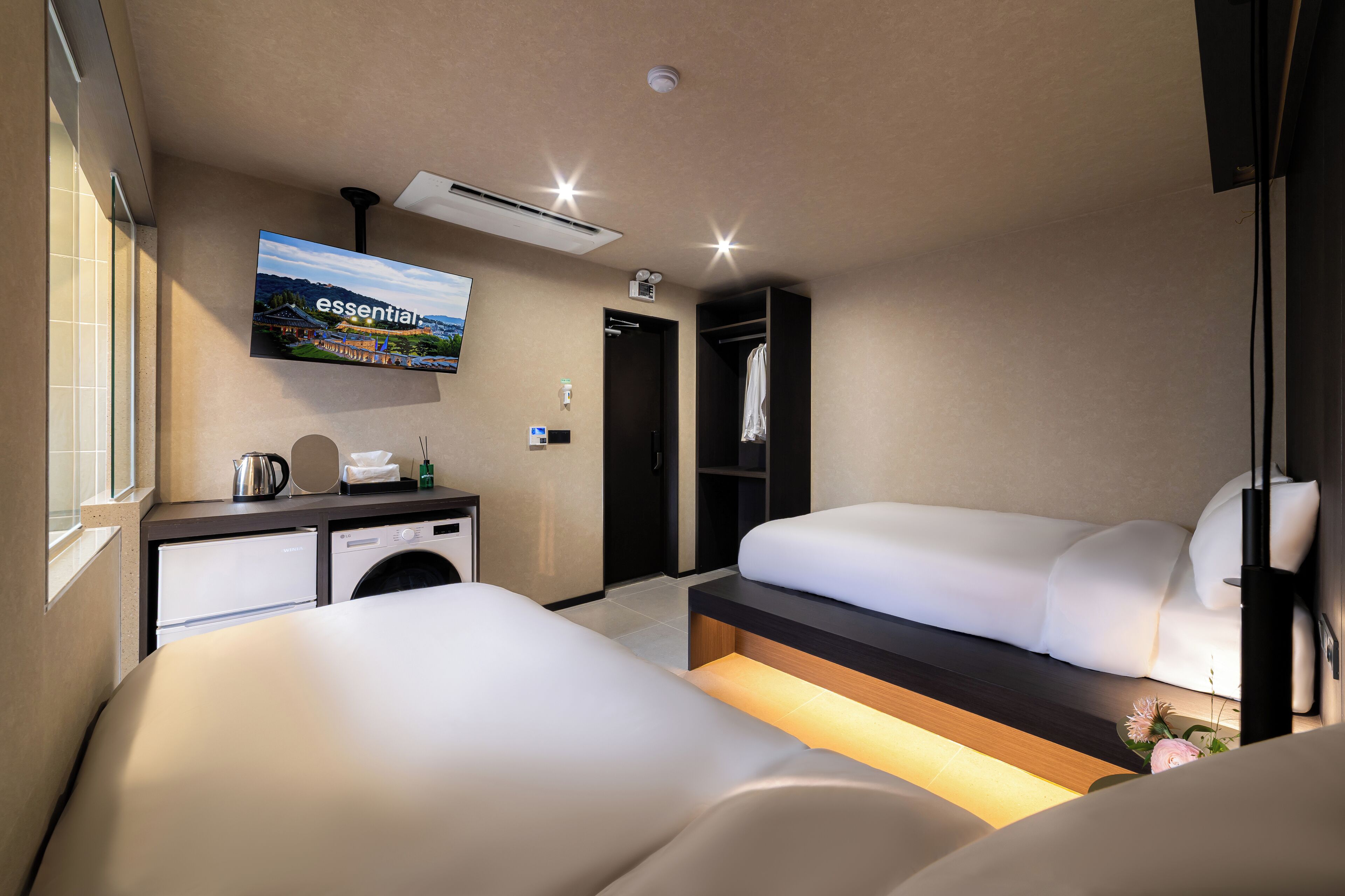 A hotel room with two beds, a TV, a washing machine, and a closet.