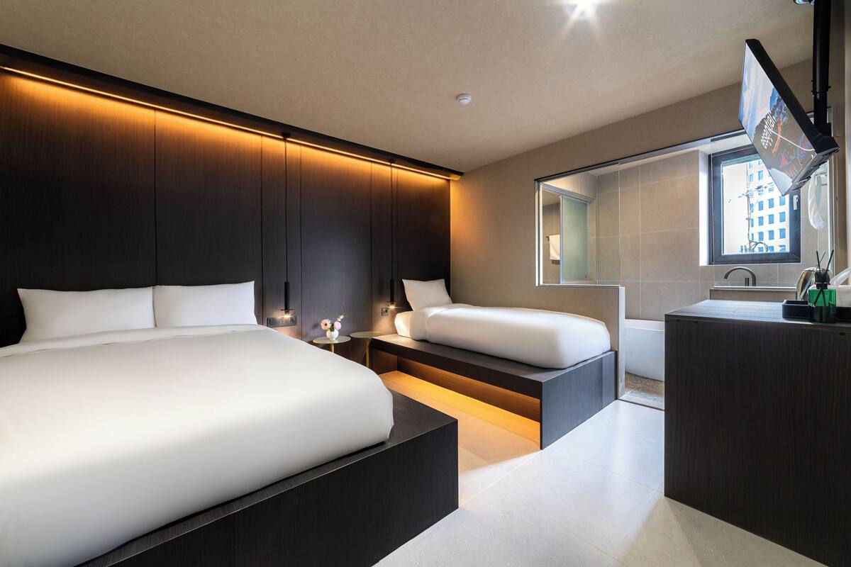 Ein modernes Hotelzimmer mit einem großen Bett, einem kleineren Bett, einem Schreibtisch und einem großen Fenster.