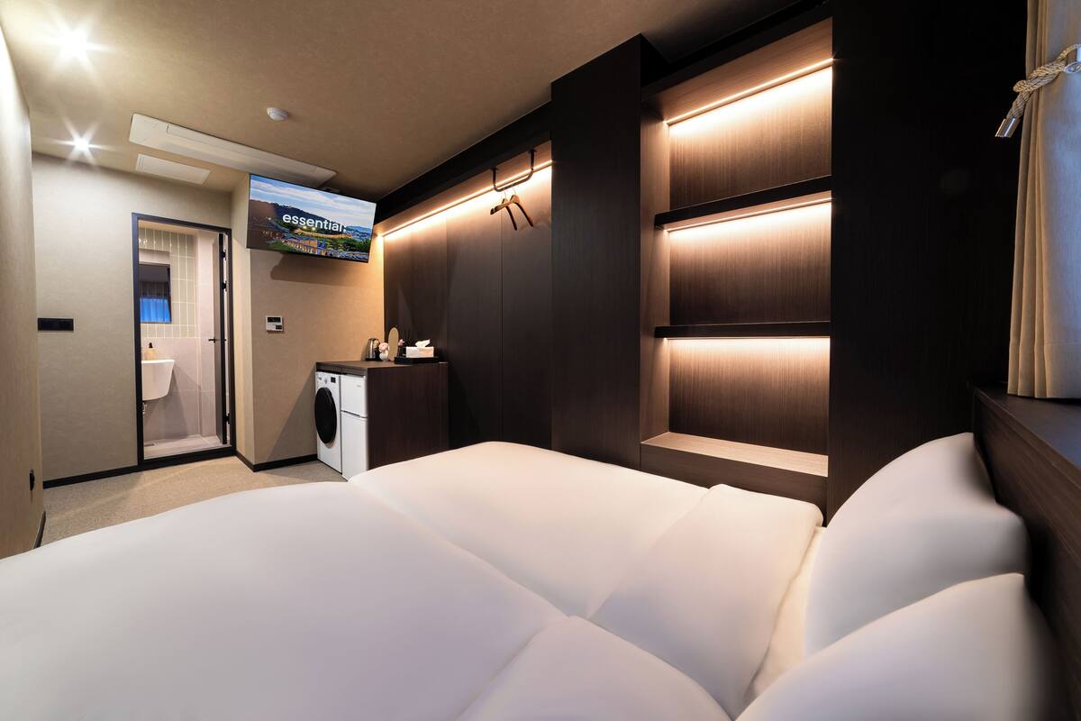 Ein Hotelzimmer mit einem großen Bett, einer Waschmaschine, einem Waschbecken und einem Fernseher, der eine Landschaft zeigt.