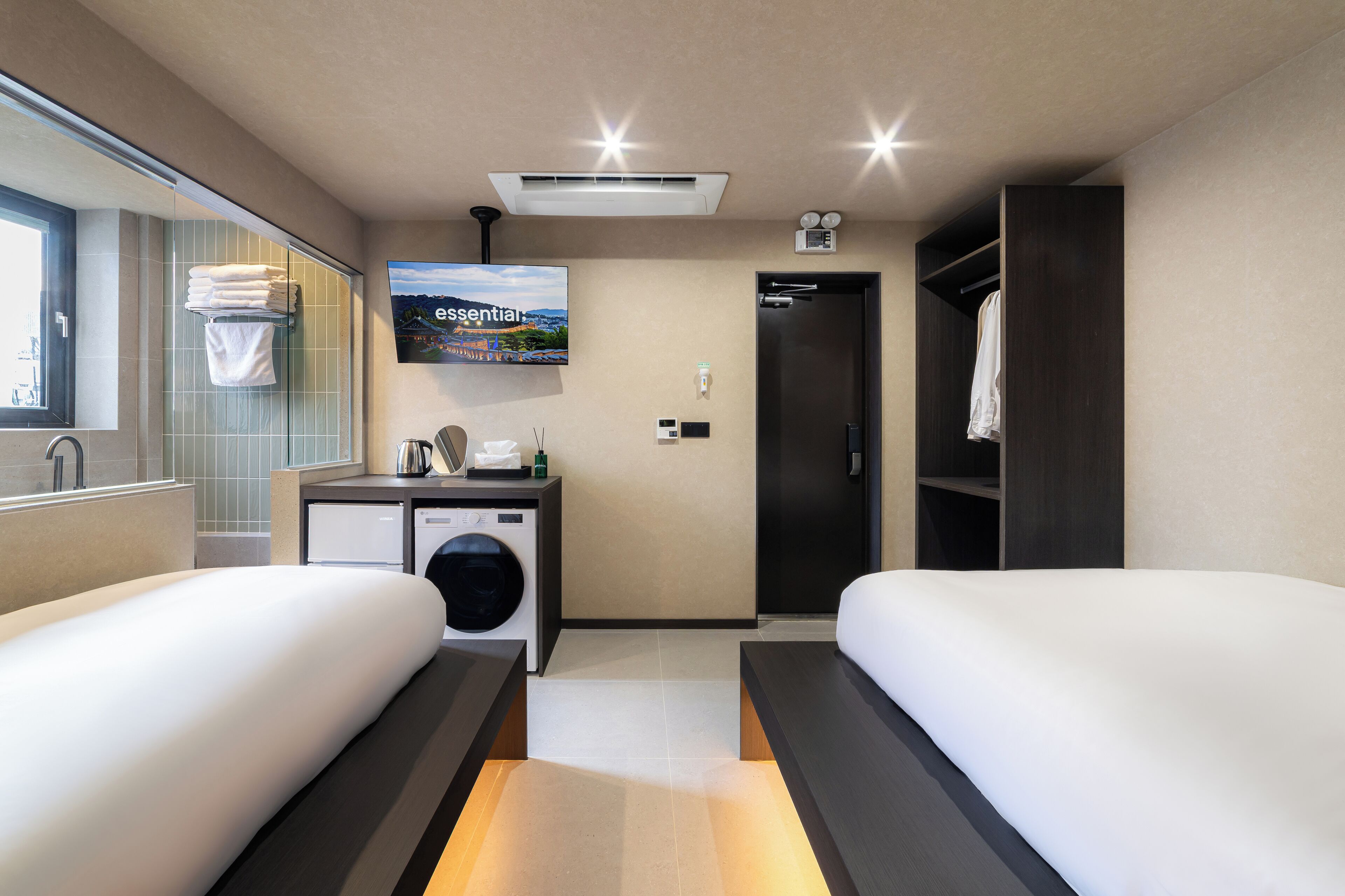 A hotel room with two beds, a washing machine, a TV, and a closet.