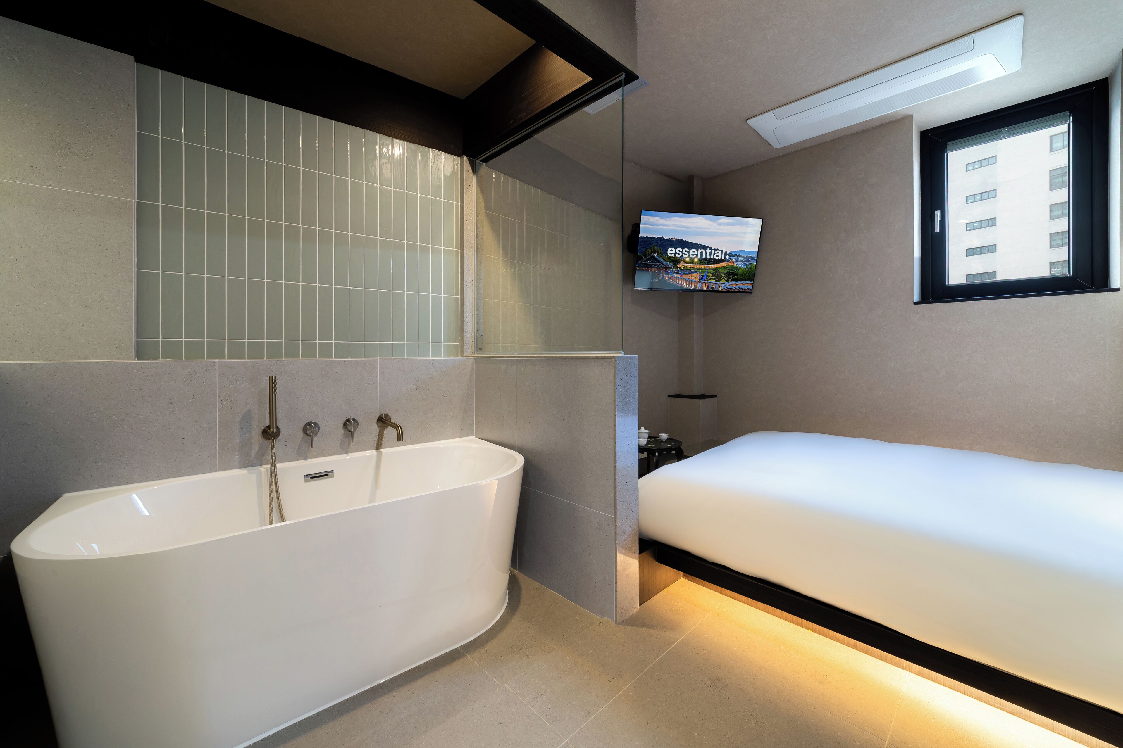 A modern bathroom with a freestanding bathtub, a bed, and a television mounted on the wall.