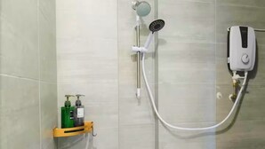 A shower with a handheld showerhead, a wall-mounted faucet, and a handheld shower pump. There is a soap dispenser and a small shelf with toiletries. - Spacious Riverview Suite @Kuching Riverine Resort (Kuching)