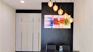 A modern dining area with a black table and chairs, a colorful abstract painting on the wall, and pendant lighting. - Spacious Riverview Suite @Kuching Riverine Resort (Kuching)