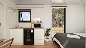 Una habitación compacta con cama, mesita de noche y una pequeña kitchenette que incluye microondas y lavabo.