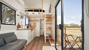 Cocina compacta con armarios blancos, sofá gris y mesa de madera con bancos.