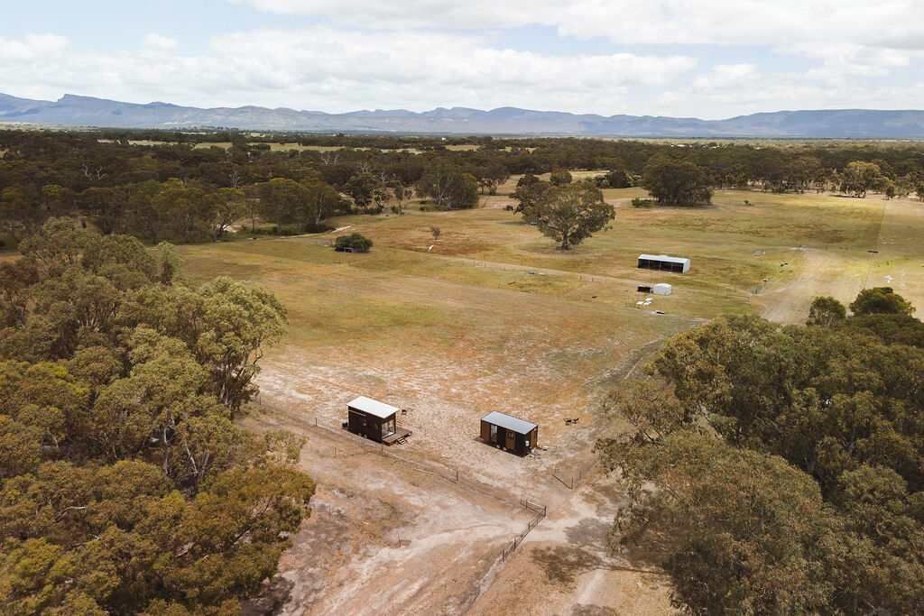 An aerial view of a rural property with two cabins and a barn, surrounded by trees and open fields.