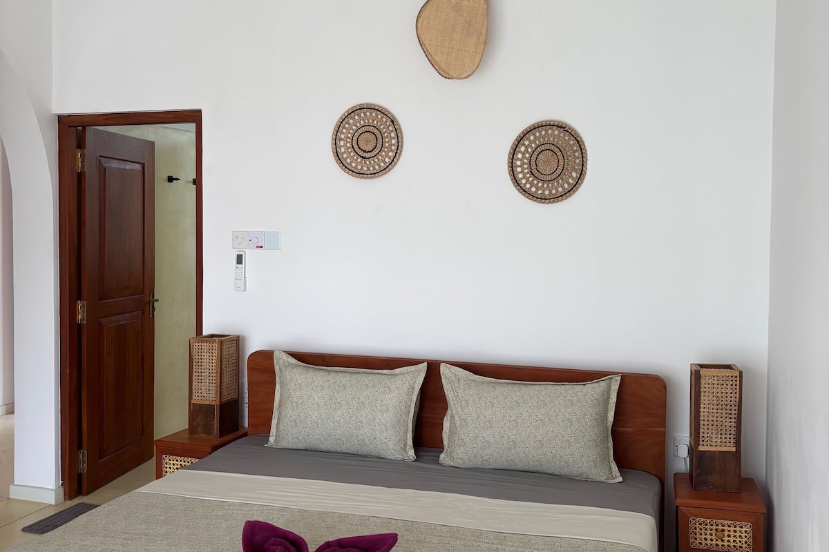 A neatly arranged bedroom with a bed, pillows, a decorative wall hanging, and a wooden door.