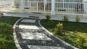Un bâtiment à deux étages doté d’un espace extérieur couvert, d’une clôture blanche et d’un jardin aménagé avec un sentier en pierre.