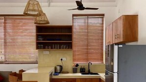 Une cuisine de taille réduite, dotée de meubles en bois, d’un réfrigérateur, d’un ventilateur de plafond et d’un coin repas avec une table et des chaises.