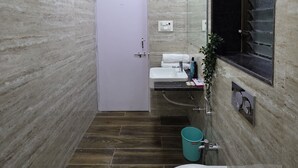 A modern bathroom with a marble wall, a white sink, a mirror, and a toilet. - Studio Apartment 103 In Malabar Hill By Florastay (Mumbai)