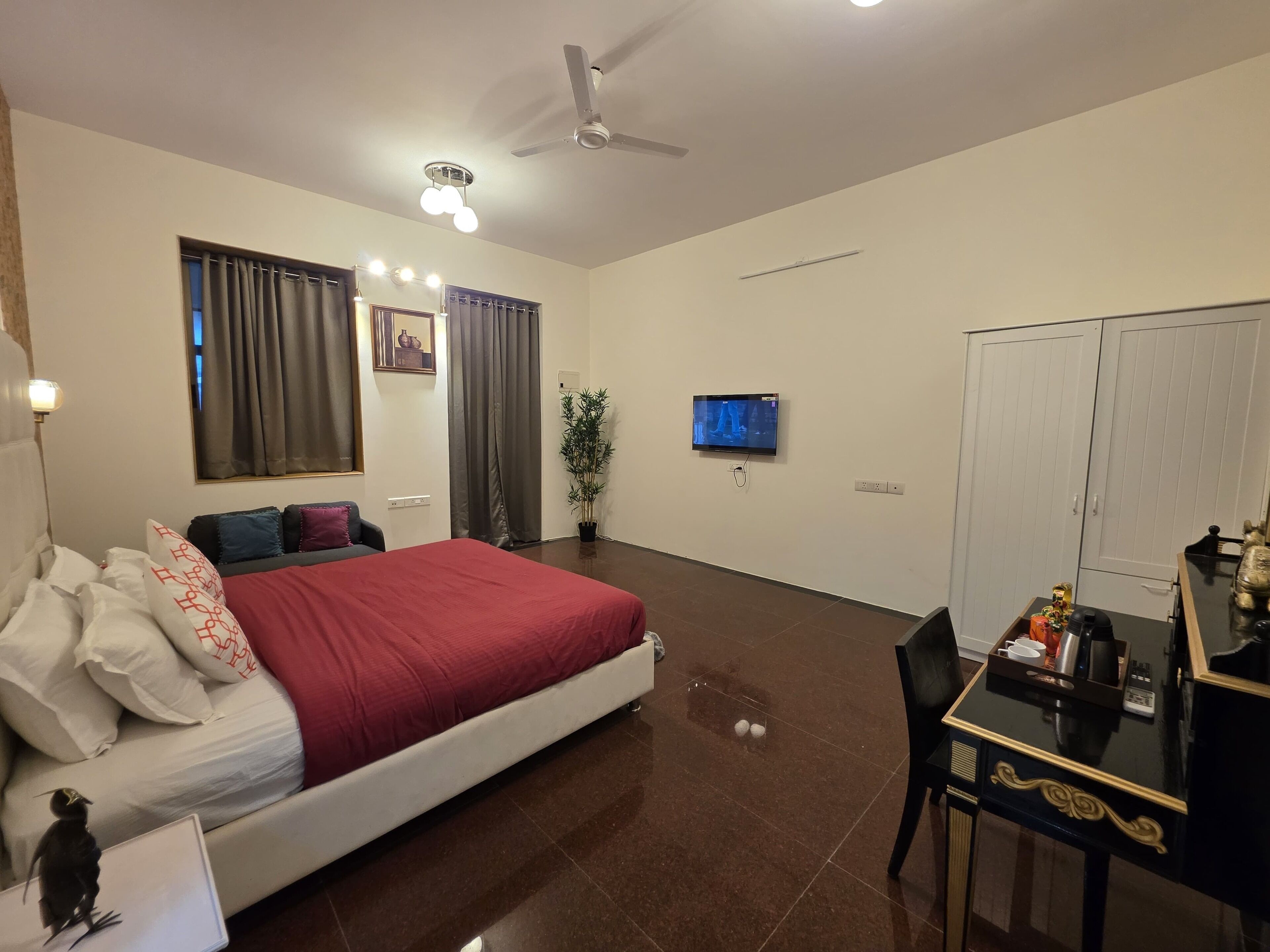 Quarto de hotel com cama, escrivaninha, televisão, ventoinha no teto e guarda-roupa.