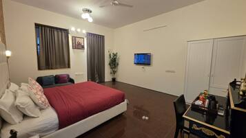 Quarto de hotel com cama, escrivaninha, televisão, ventoinha no teto e guarda-roupa.