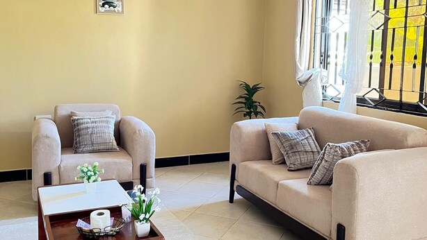 Un salon aux murs de couleur beige, avec deux canapés, une table basse et une fenêtre agrémentée de rideaux.