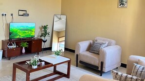Un salon avec un canapé beige, une table basse ornée de fleurs, un téléviseur et un ventilateur de plafond.