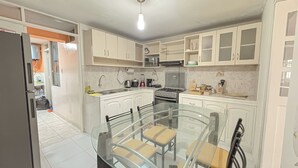 Une cuisine moderne avec des meubles blancs, une cuisinière à gaz, un four à micro-ondes et une table à manger en verre, accompagnée de chaises.