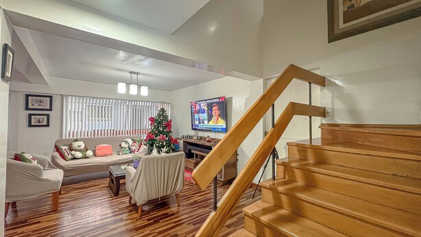 Un salon avec un escalier en bois, un sapin de Noël, un canapé et un téléviseur.