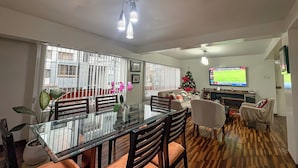 Un salon moderne avec une table à manger en verre, des chaises en bois, un téléviseur et un sapin de Noël.