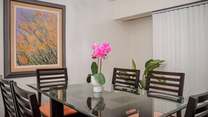 Un coin repas avec une table en verre, quatre chaises en bois, un tableau encadré au mur et une plante en pot.
