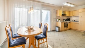 Un coin repas avec une table ronde et quatre chaises, une cuisine avec des meubles en bois clair et un radiateur situé à gauche.