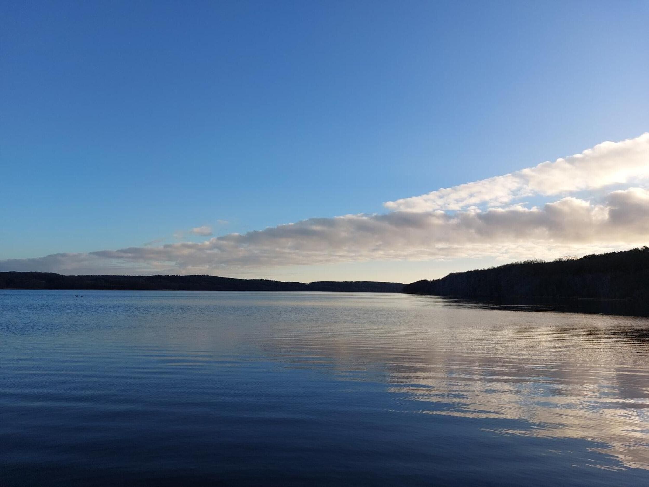 Un lago tranquilo con cielo despejado y colinas a lo lejos.