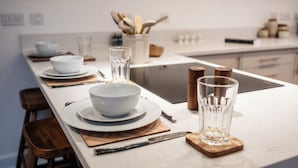 Eine moderne Küche mit weißen Arbeitsplatten, Holzstühlen und einer zentralen Kochinsel mit Schüssel und Glas.